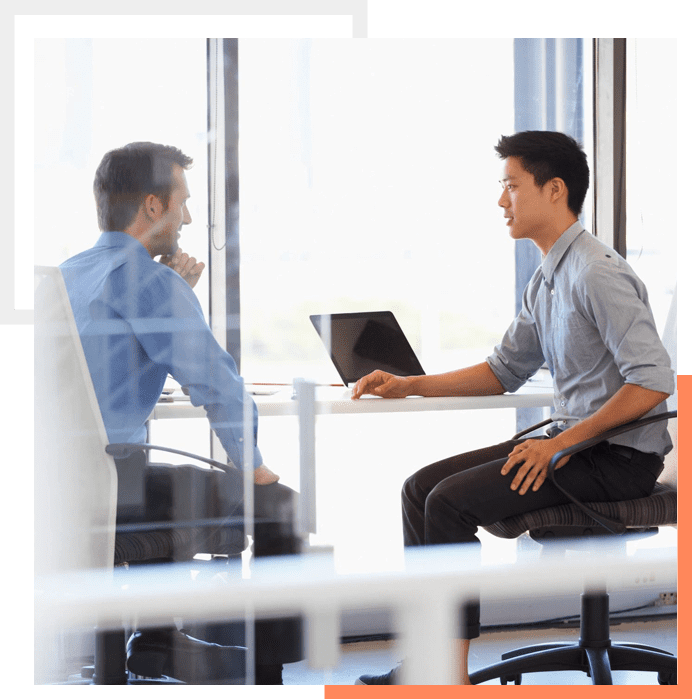 Two men sitting at a table with laptops.